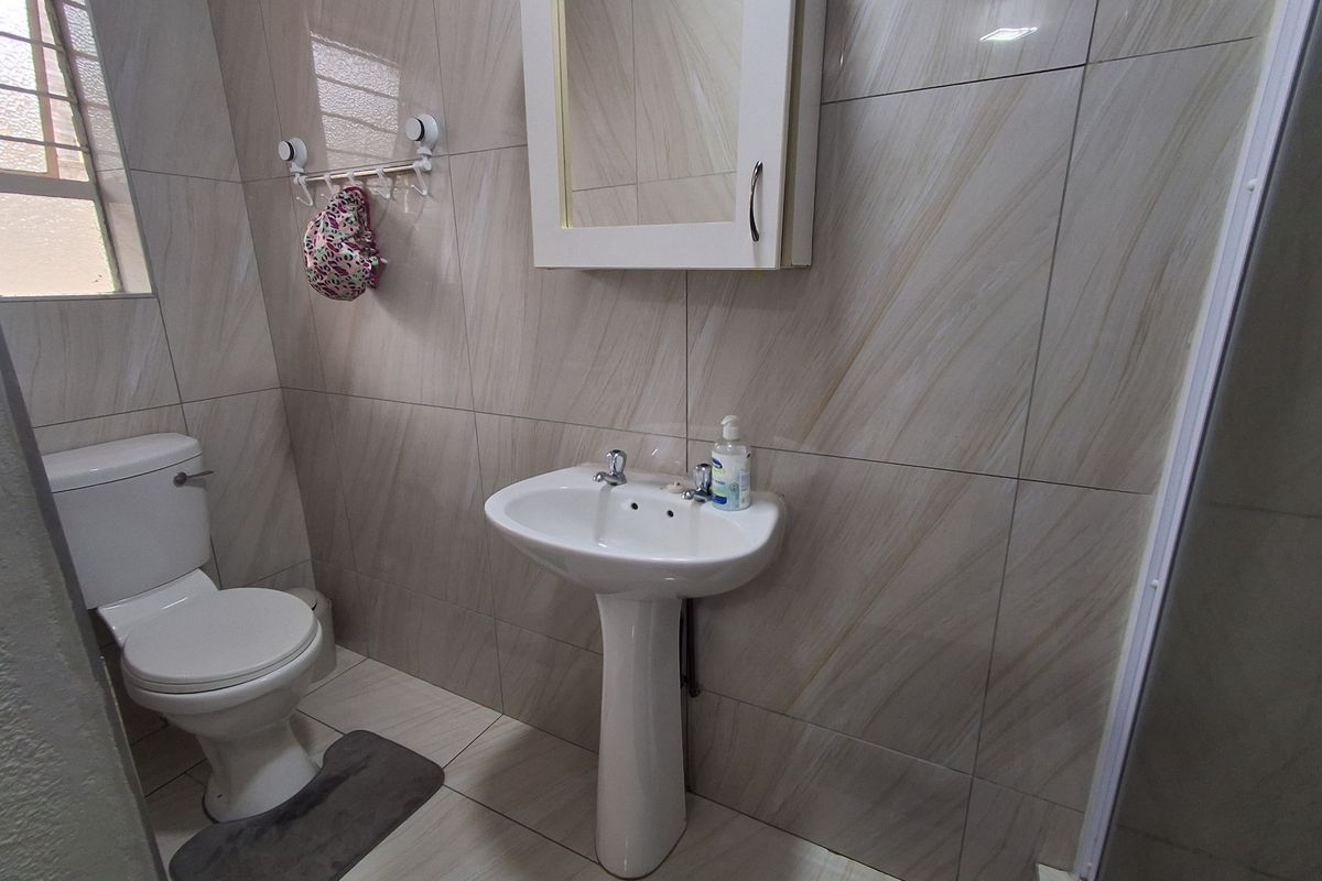 A functional bathroom featuring a pedestal basin, a wall-mounted medicine cabinet, a toilet, and floor-to-ceiling tiled walls.