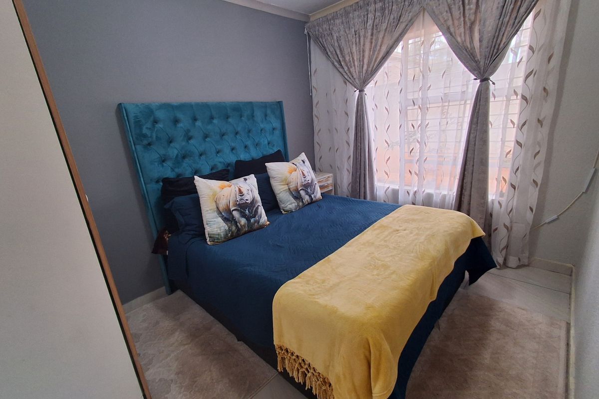 A well-maintained bedroom featuring neutral wall tones, tiled flooring, and large windows with fitted curtain tracks.