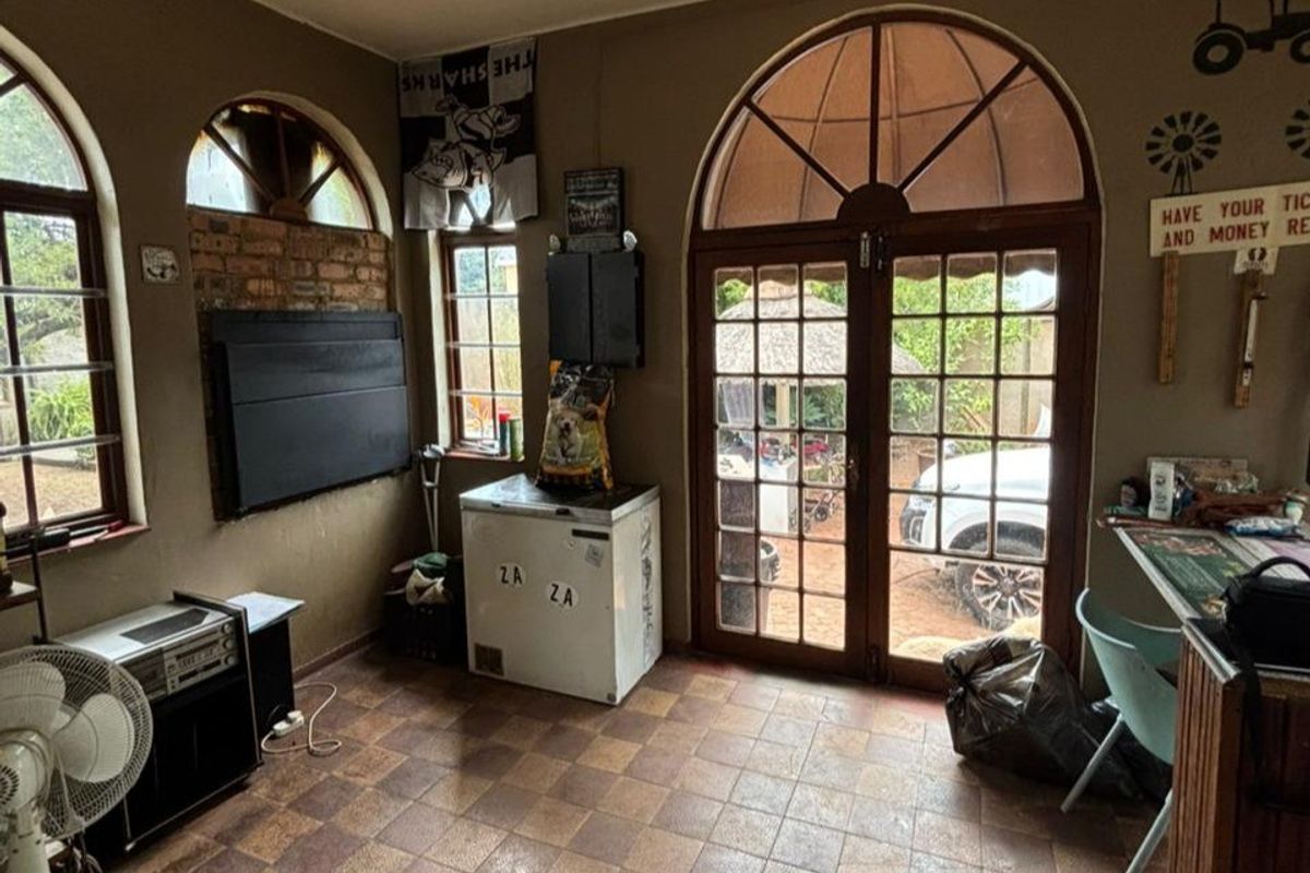 A multi-purpose living area featuring arched windows, double glass doors leading to the exterior, and tiled flooring.
