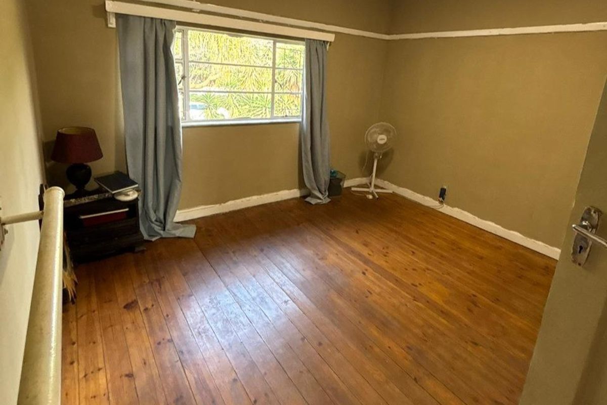A bedroom featuring original timber flooring, neutral wall tones, and a window providing natural light.