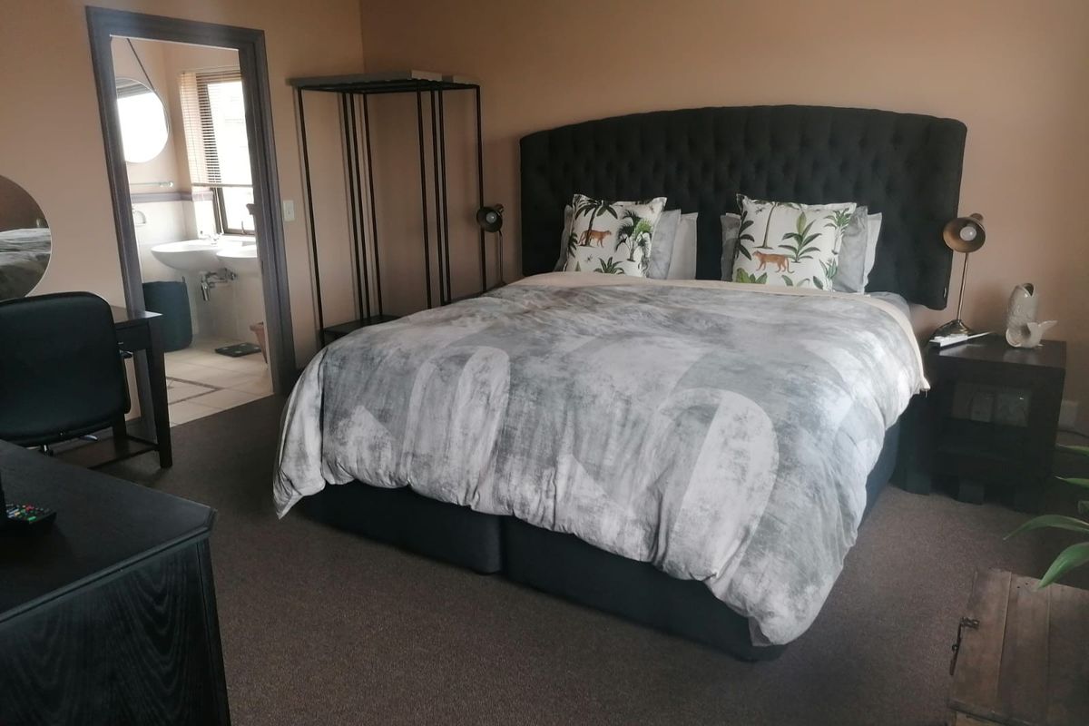 A spacious bedroom featuring neutral wall tones, carpeted flooring, and an adjoining en-suite bathroom with a double vanity.