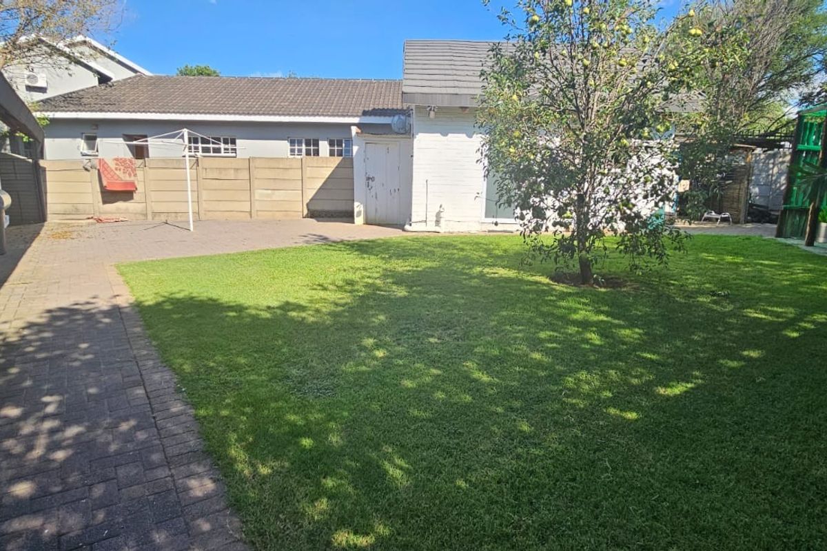 A spacious rear garden featuring a paved patio area, a well-maintained lawn, and perimeter walling.