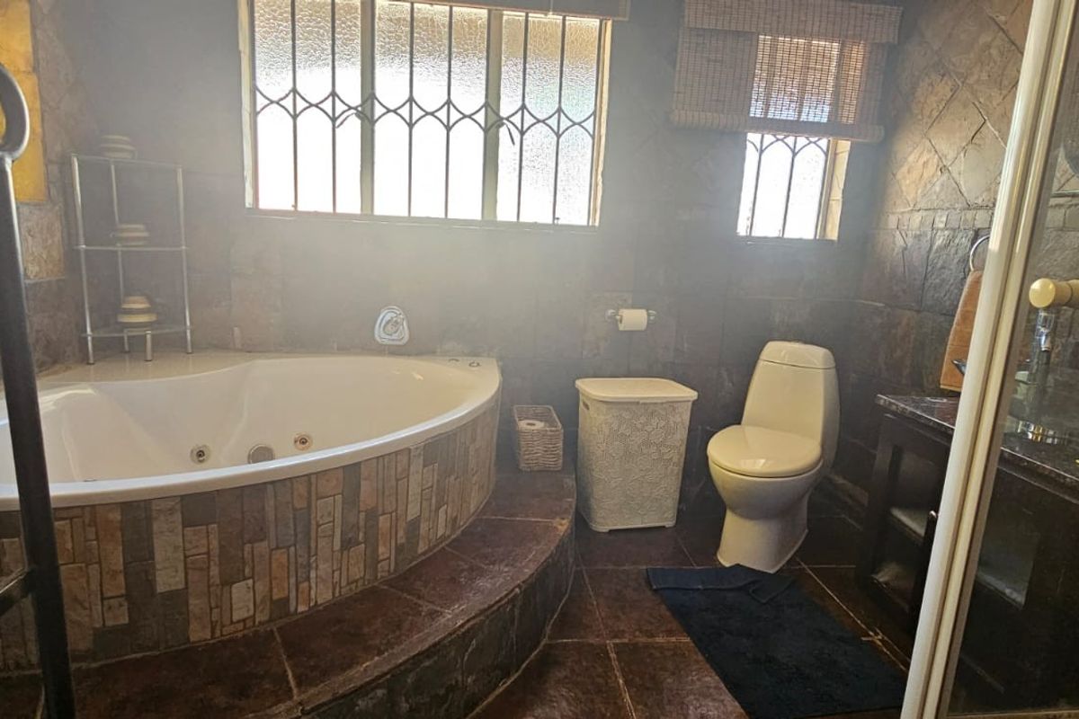 A bathroom featuring a corner jetted bathtub, a toilet, and a vanity unit with dark stone-style wall and floor tiling.