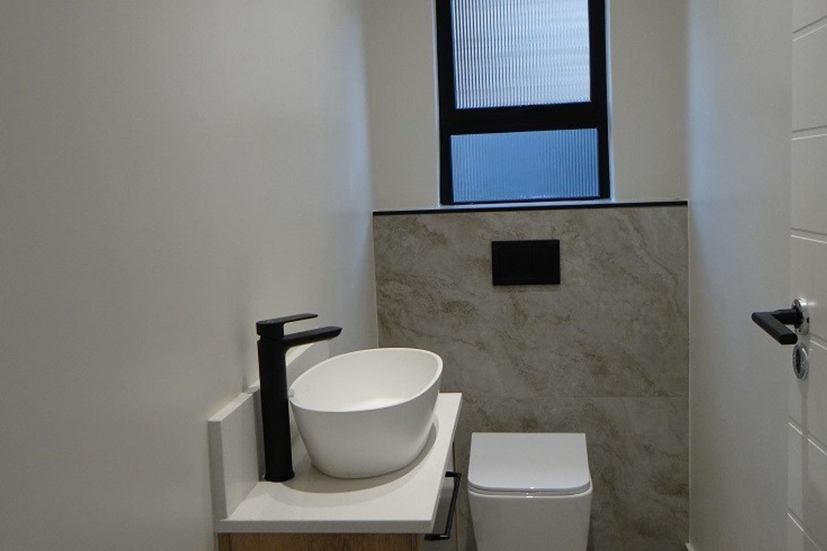 A modern guest bathroom featuring a wall-mounted vanity with a vessel sink, matte black tapware, and a wall-hung toilet with tiled feature wall.