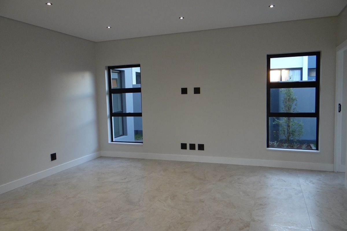 A bright, modern living room featuring neutral tiled flooring, recessed downlighting, and large windows with dark frames, providing a clean and contemporary aesthetic.