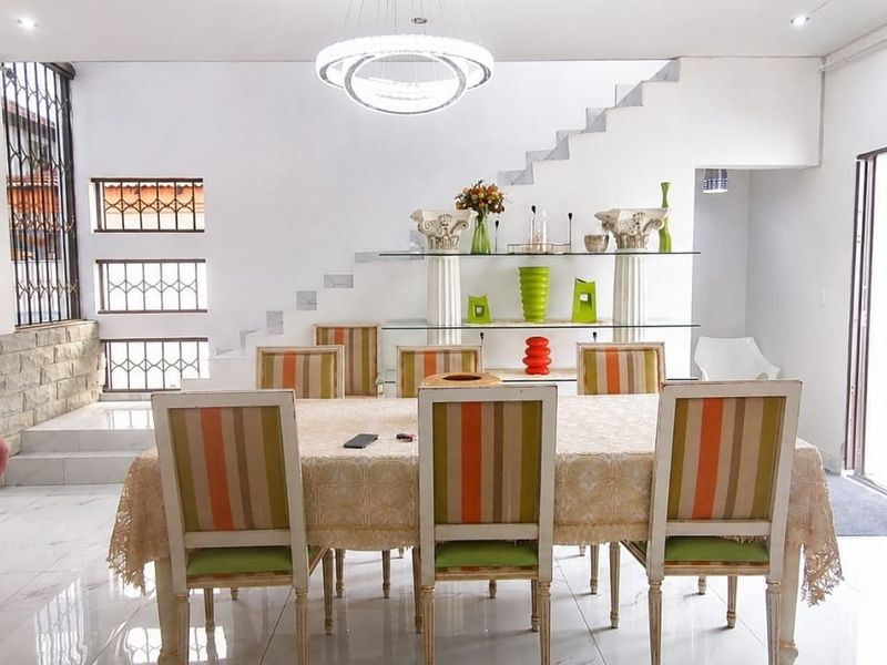 Spacious dining area featuring polished tiled floors, a modern chandelier, and a stone feature wall with an integrated staircase.