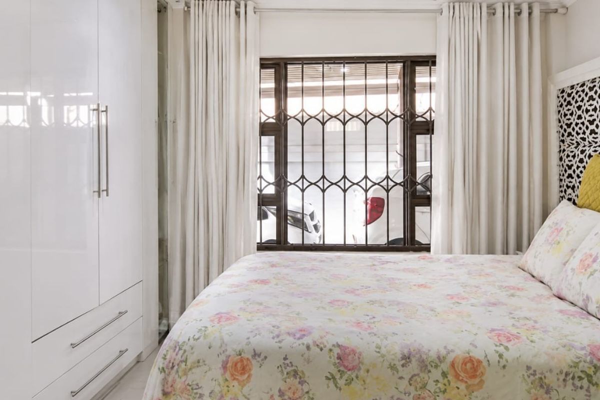 A well-maintained bedroom featuring modern white built-in cupboards and a window fitted with security bars.
