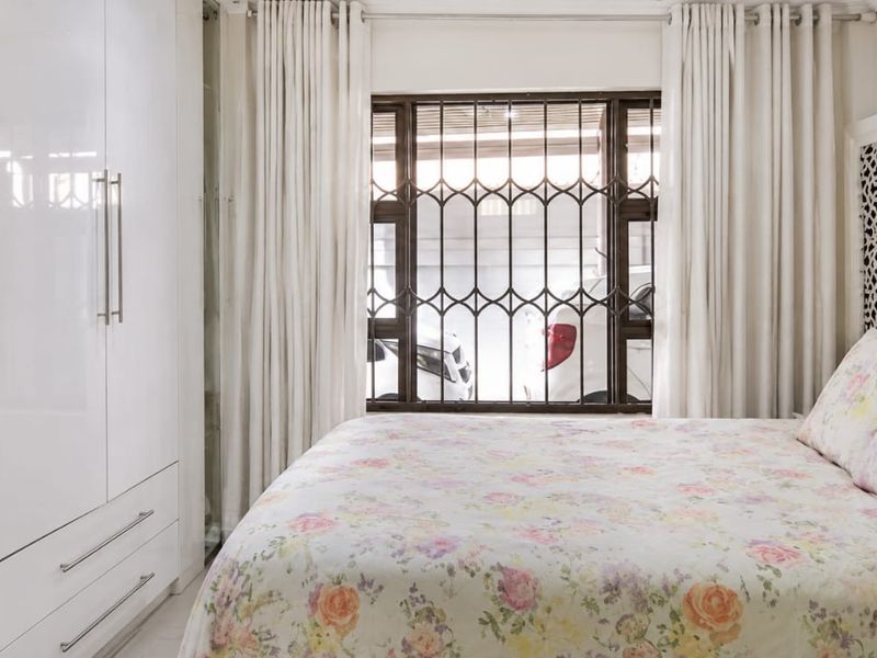 A well-maintained bedroom featuring modern white built-in cupboards and a window fitted with security bars.