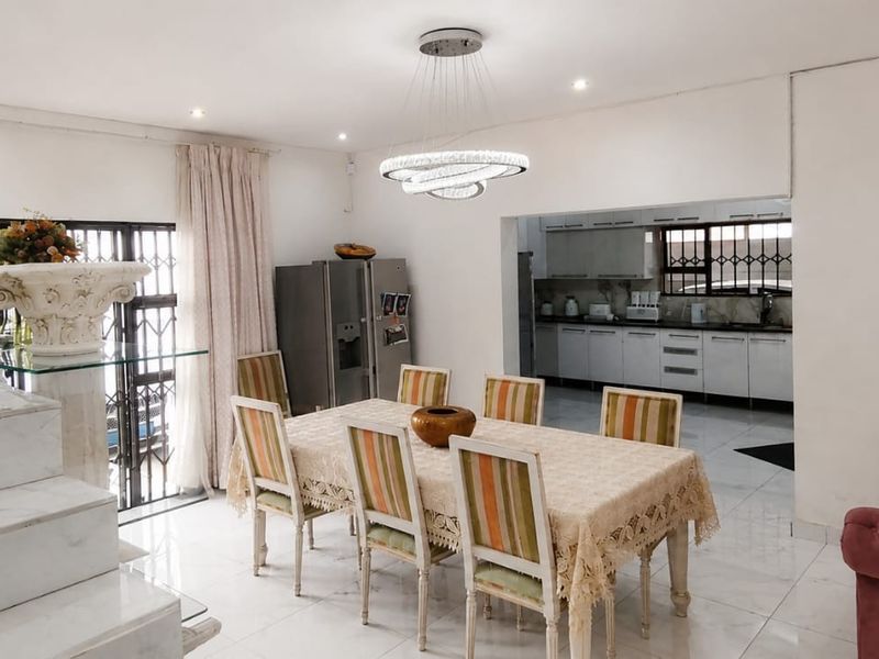 Open plan dining and kitchen area featuring marble staircase, modern lighting, and tiled flooring, creating a bright and functional living space.