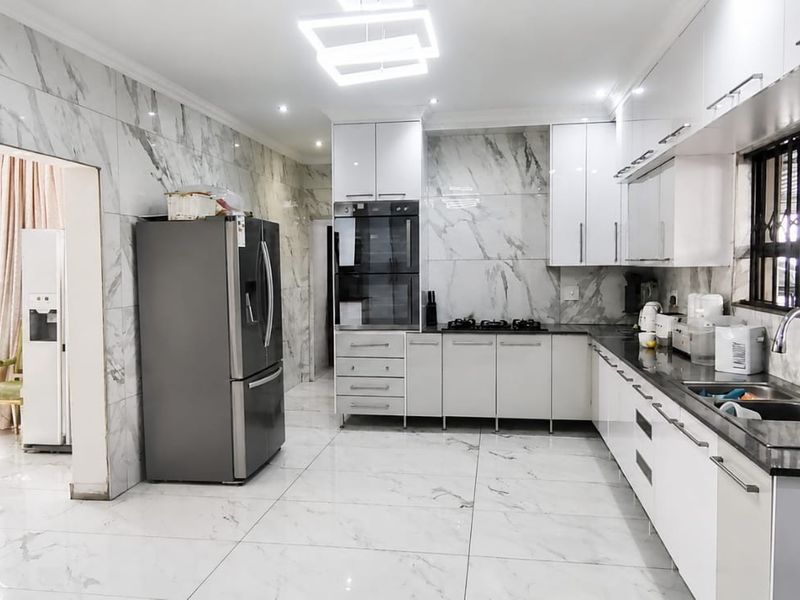 Modern kitchen featuring marble-look wall and floor tiles, sleek white cabinetry, built-in oven, gas hob, and high-quality finishes throughout.