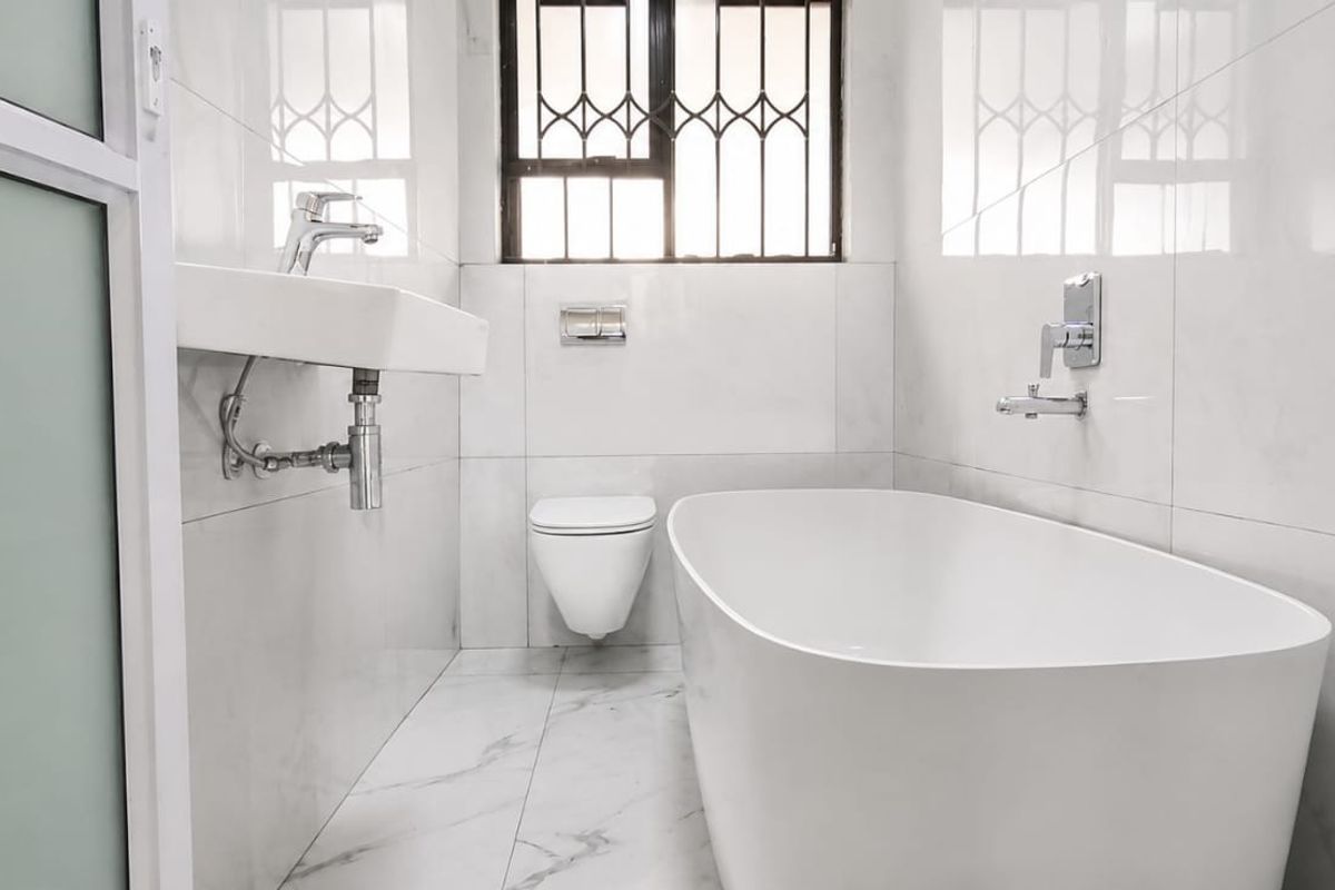 Modern, minimalist bathroom featuring a sleek freestanding bathtub, wall-hung toilet, and contemporary wall-mounted basin with marble-look tiling throughout.