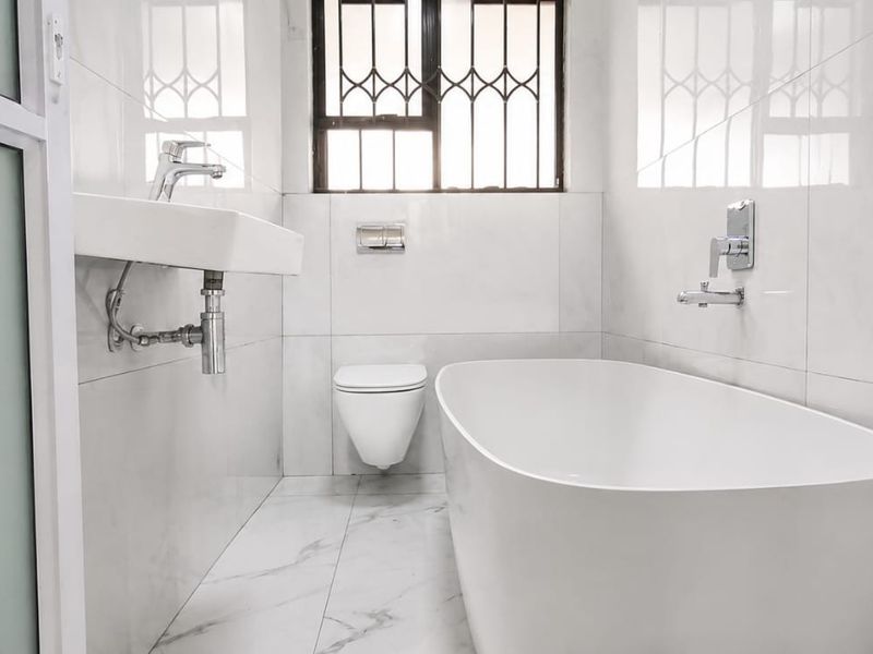 Modern, minimalist bathroom featuring a sleek freestanding bathtub, wall-hung toilet, and contemporary wall-mounted basin with marble-look tiling throughout.
