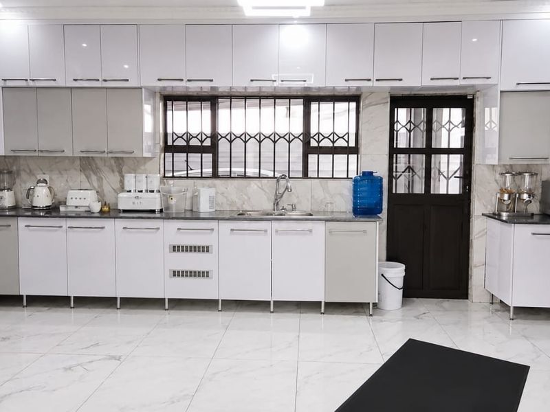 Modern kitchen featuring high-gloss white cabinetry, marble-look wall and floor tiles, and a functional layout with integrated sink and security features.