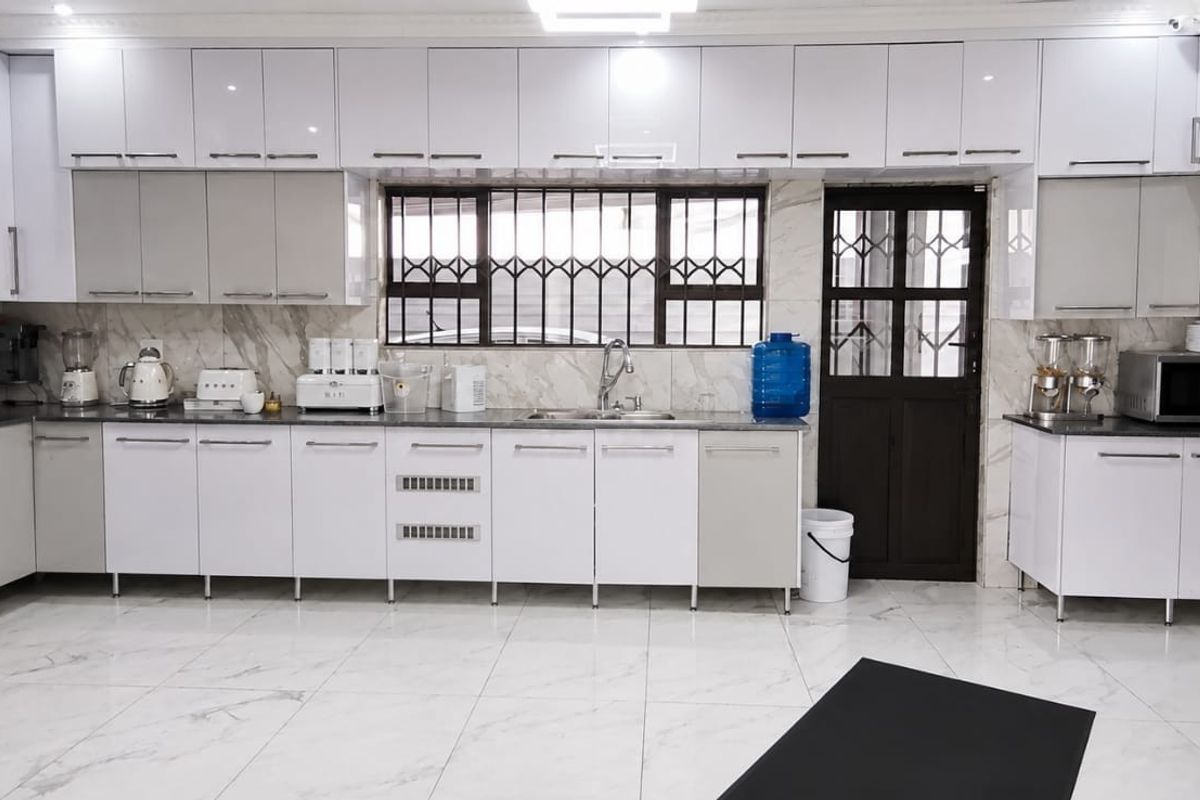 Modern kitchen featuring high-gloss white cabinetry, marble-look wall and floor tiles, and a functional layout with integrated sink and security features.