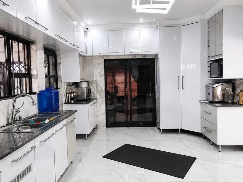 Modern kitchen featuring high-gloss white cabinetry, marble-look tiled floors and walls, granite countertops, and integrated appliances with ample storage space.