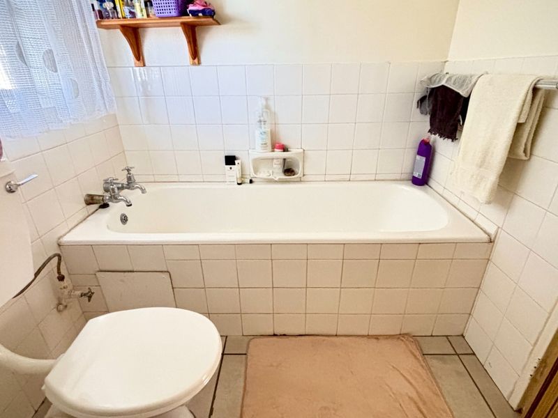 A functional bathroom featuring a standard bathtub, toilet, and tiled finishes, offering potential for modernization and cosmetic updates.