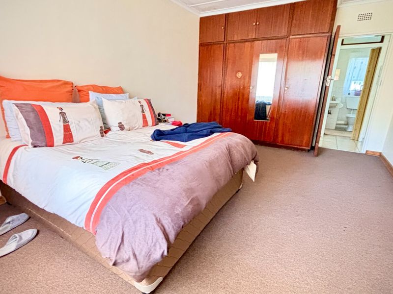 Spacious bedroom featuring built-in wooden wardrobes, carpeted flooring, and direct access to an en-suite bathroom.