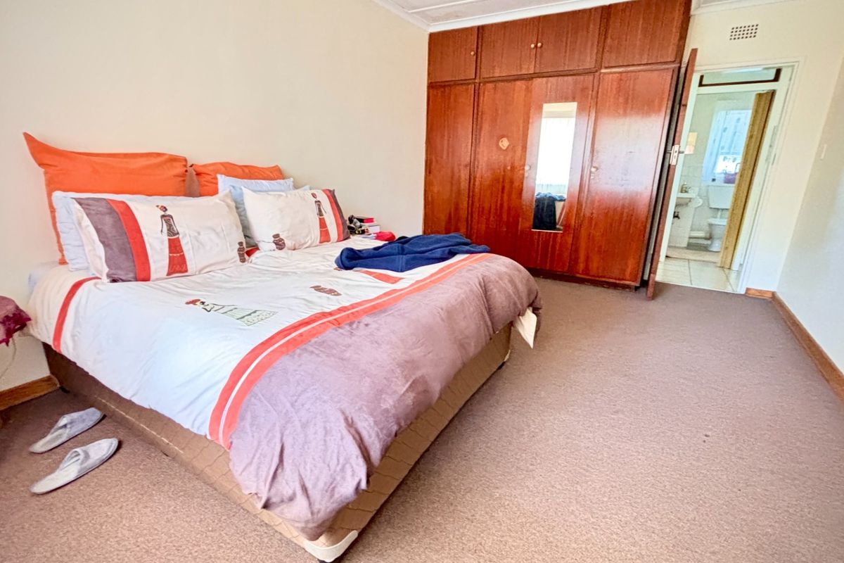 Spacious bedroom featuring built-in wooden wardrobes, carpeted flooring, and direct access to an en-suite bathroom.