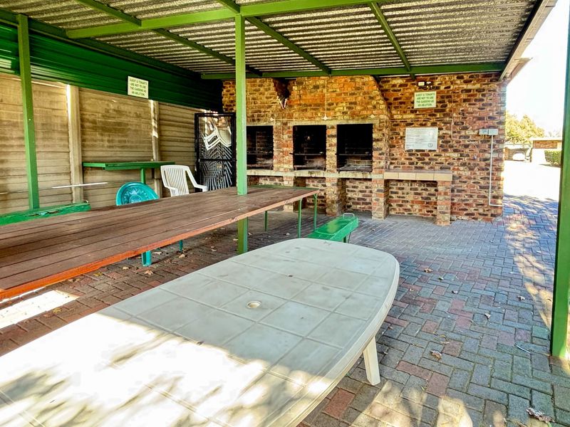 Covered outdoor entertainment area featuring a built-in brick braai, paved flooring, and a durable steel-framed roof structure.