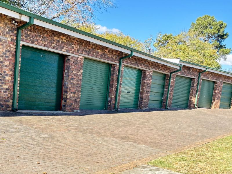 A row of secure brick-built garages featuring green roller doors and a paved driveway area.