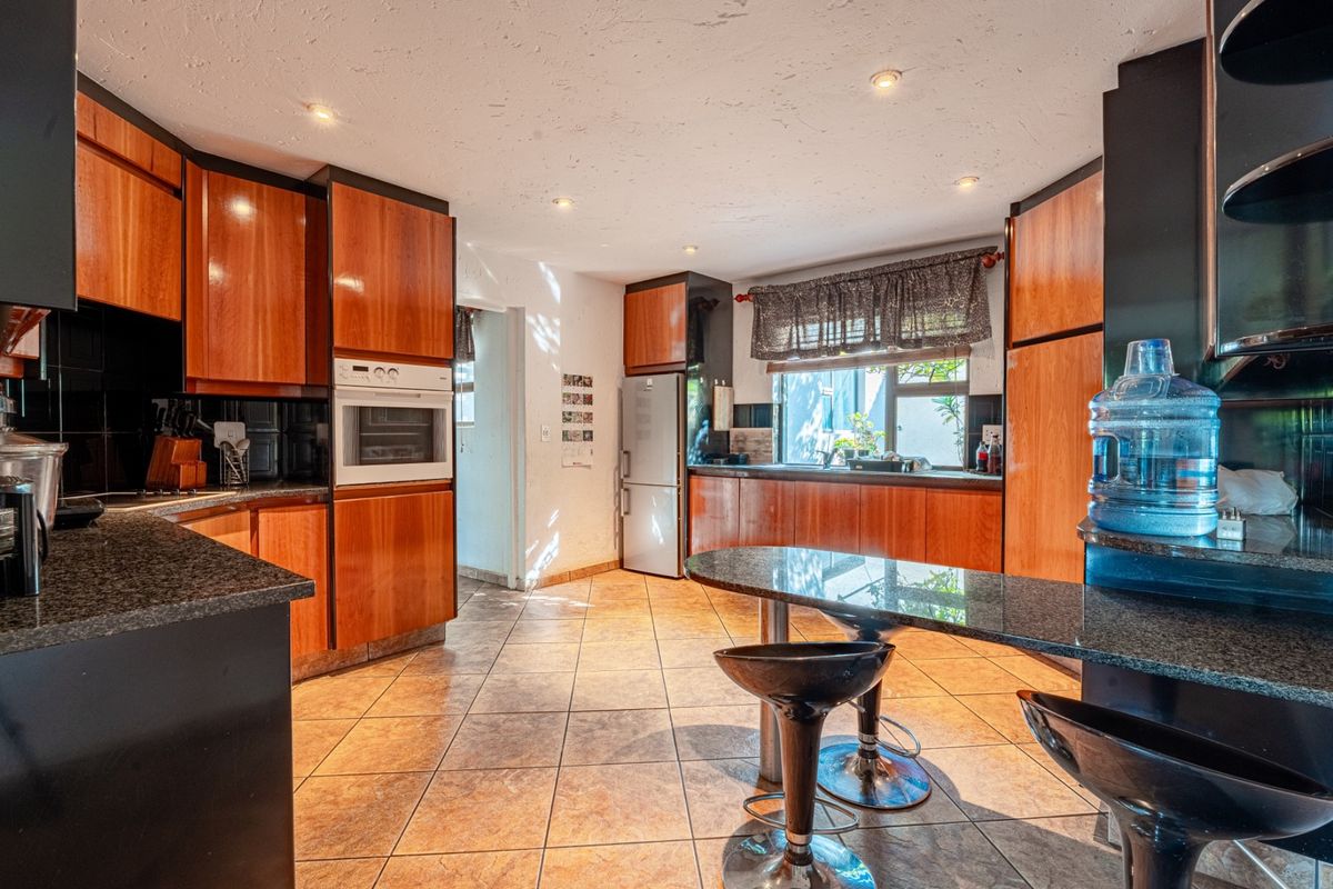 A spacious kitchen featuring wood-veneer cabinetry, granite countertops, a built-in oven, and a breakfast bar area with tiled flooring.