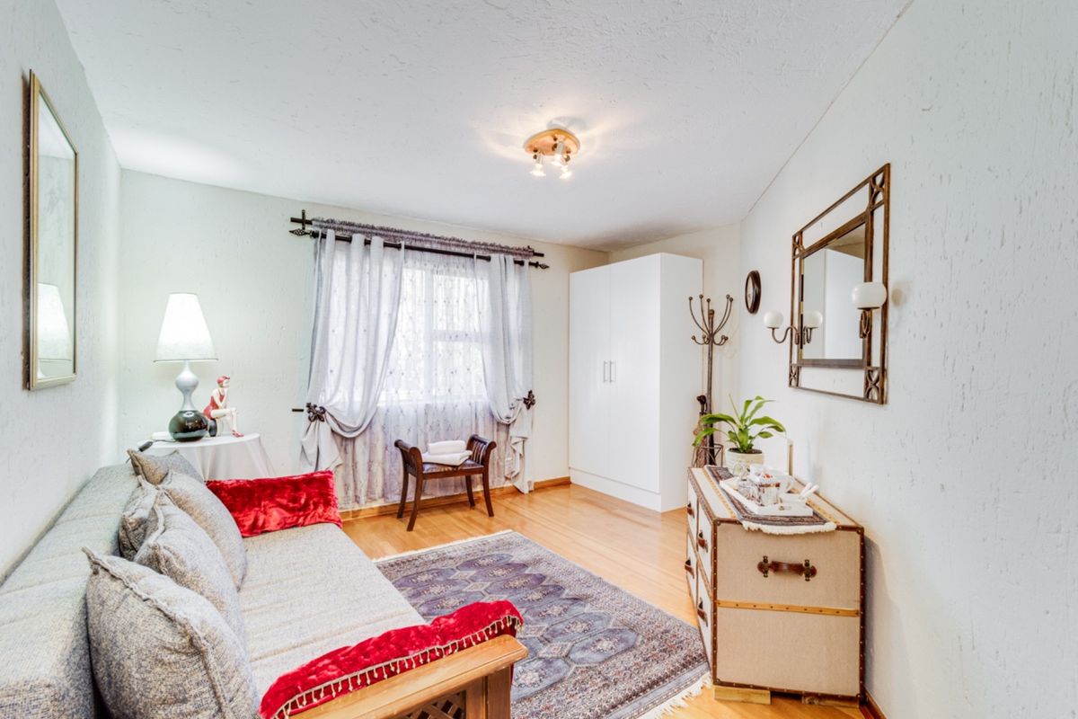 A cozy bedroom featuring light wood flooring, a built-in white wardrobe, and a window with curtain treatments.
