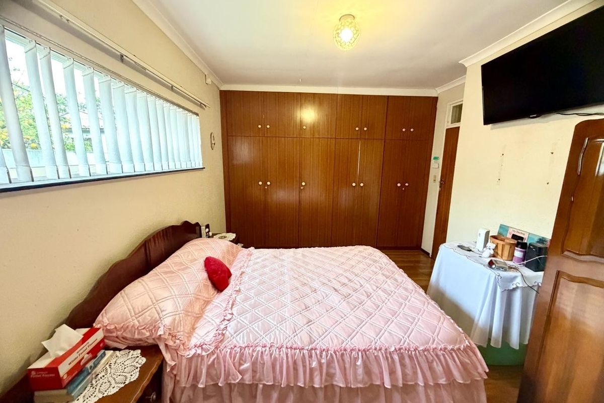 A bedroom featuring built-in wooden wardrobes, vertical blinds, and a ceiling light fixture.