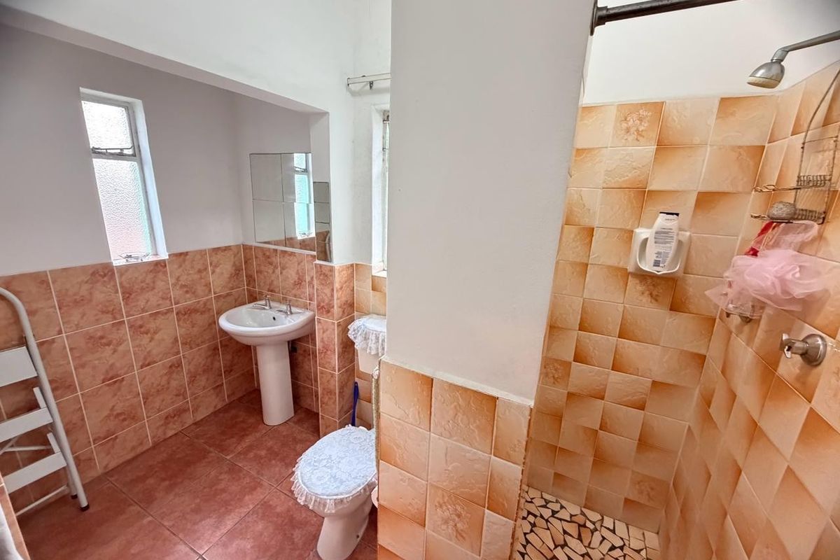 A dated bathroom featuring a pedestal basin, toilet, and a walk-in shower with orange-toned ceramic wall tiles and mosaic floor tiling.