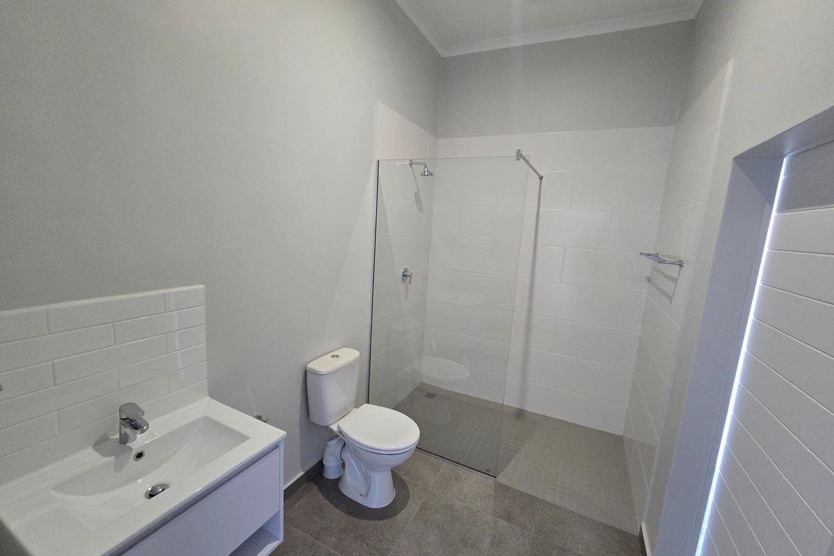 Modern bathroom featuring a walk-in shower with glass screen, vanity with basin, and toilet, finished with neutral wall and floor tiles.