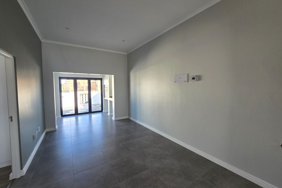 A bright, empty living area featuring large format floor tiles, neutral walls, and bi-fold doors leading to an outdoor space.