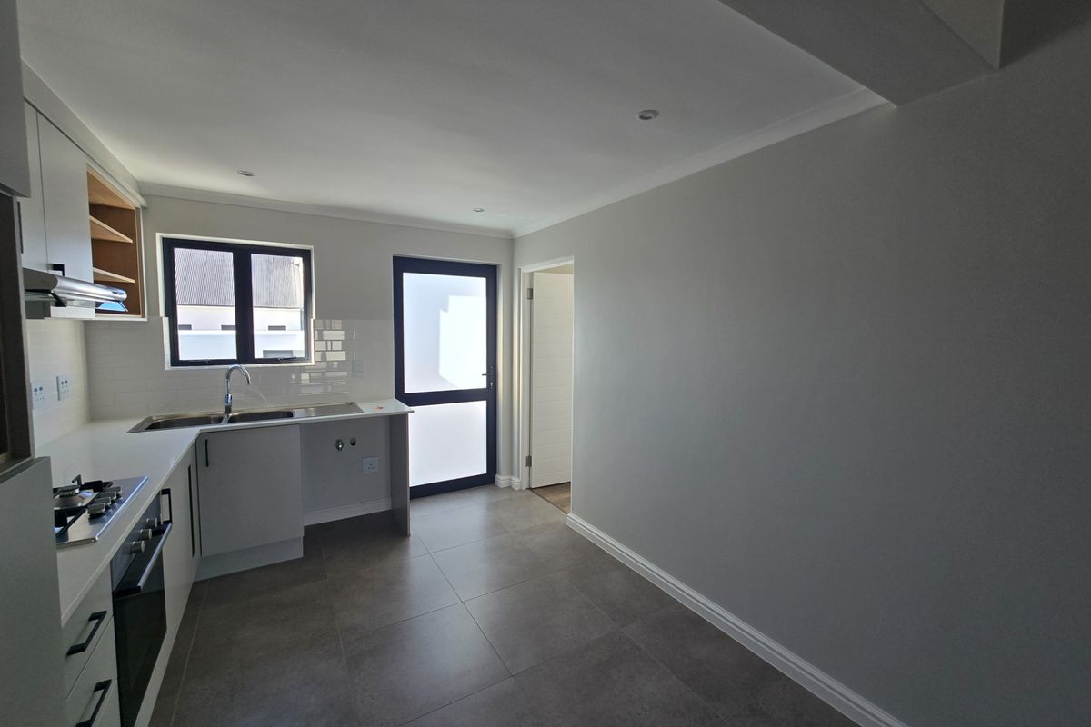 A modern, clean kitchen featuring built-in cabinetry, stainless steel appliances, subway tile backsplash, and neutral tiled flooring with direct access to the exterior.