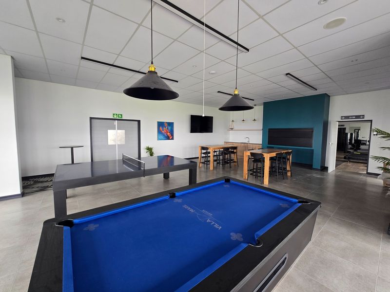 Spacious clubhouse area featuring tiled flooring, a built-in kitchenette, and a built-in braai, designed for social gatherings and recreational activities.