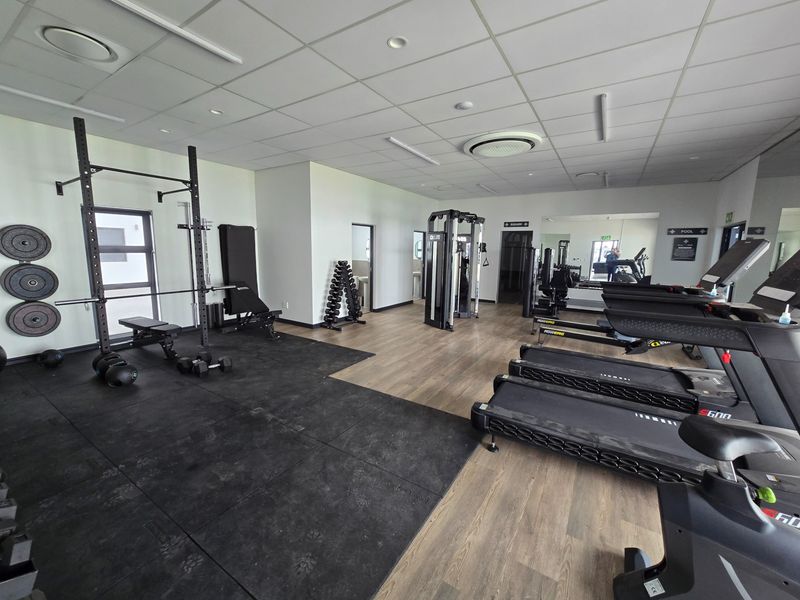 A well-maintained communal gym facility featuring a mix of rubber and laminate flooring, mirrored walls, and integrated ceiling lighting.
