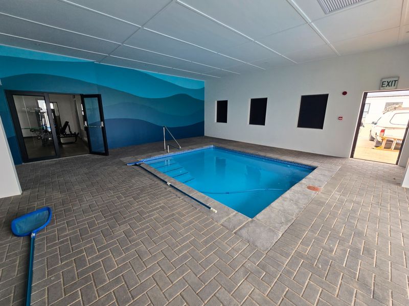 Indoor swimming pool area featuring a tiled surround, pool steps with handrail, and a clean, modern aesthetic with blue wave-patterned wall accents.