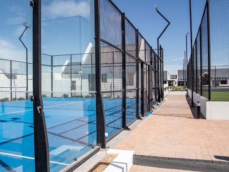 A well-maintained outdoor padel court featuring glass and mesh perimeter fencing, integrated floodlights, and adjacent paved walkways.