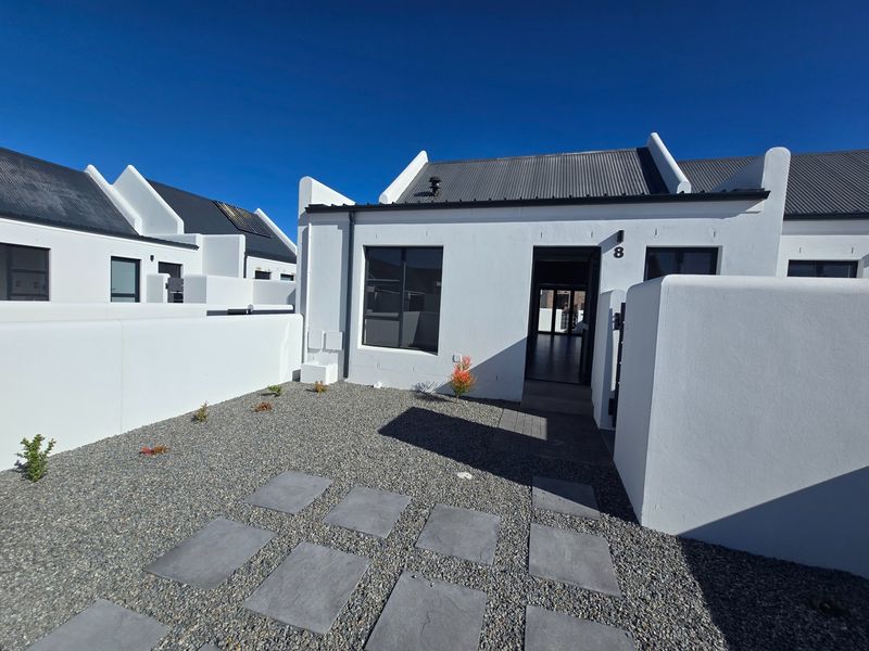 A modern, well-maintained front facade featuring a clean white exterior, corrugated metal roof, and a low-maintenance gravel garden with a paved entrance path.