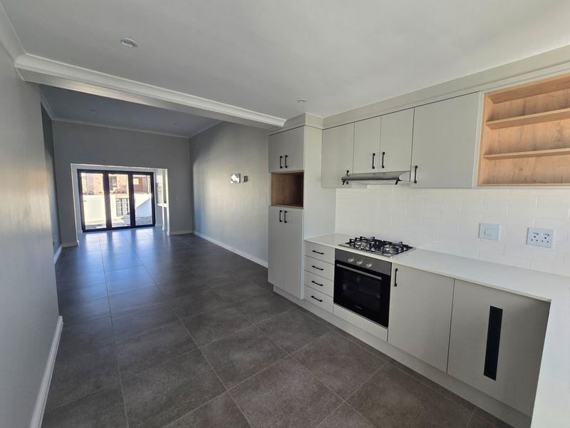 Modern open-plan kitchen and living area featuring sleek cabinetry, built-in appliances, tiled flooring, and large sliding doors leading to the exterior.