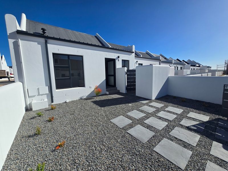 A modern, well-maintained front exterior featuring a clean white facade, corrugated metal roof, and a low-maintenance gravel garden with stone paving.