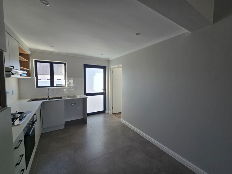 A modern, clean kitchen featuring built-in cabinetry, stainless steel appliances, subway tile backsplash, and neutral tiled flooring with direct access to the exterior.