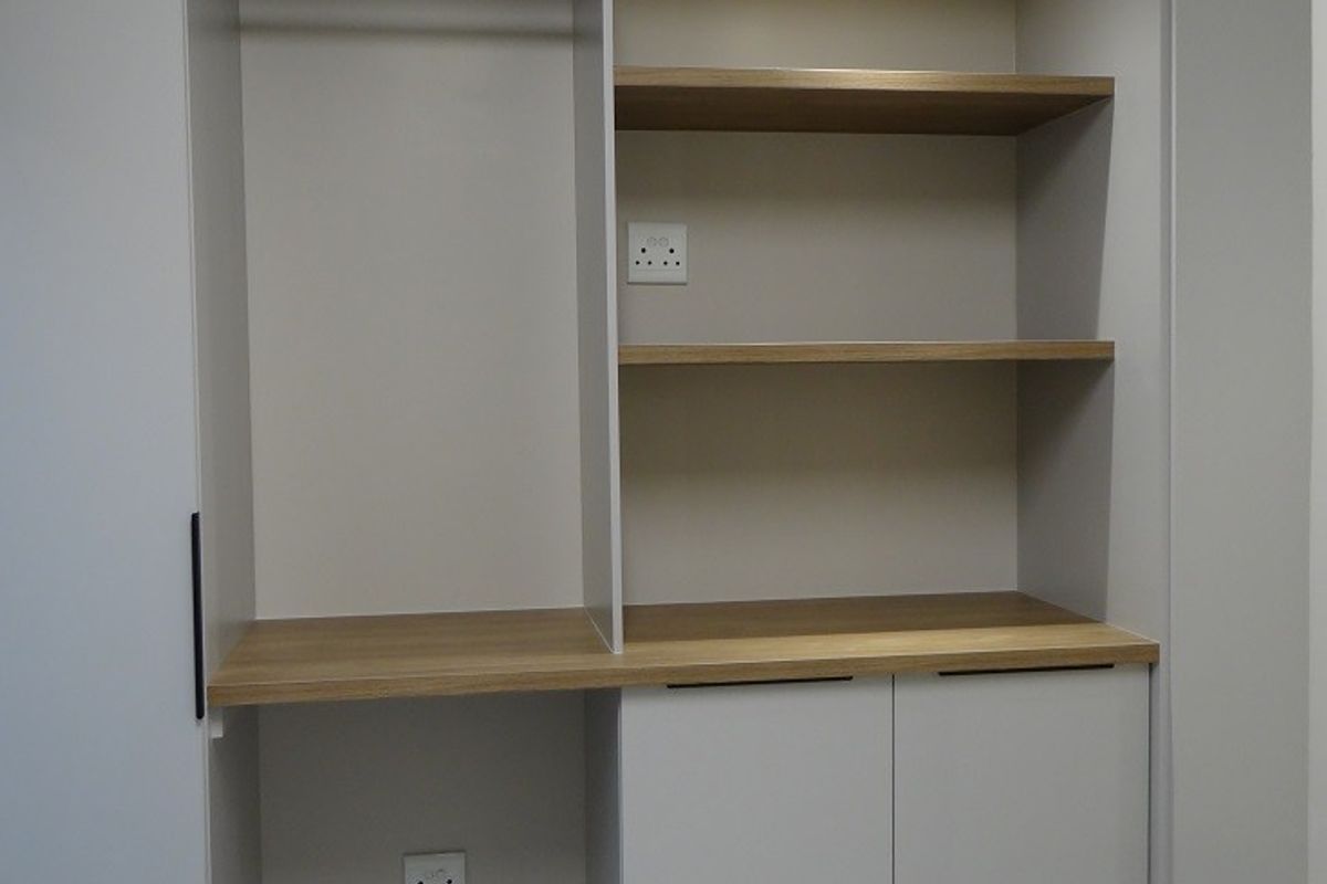 A modern built-in storage unit featuring open shelving, a hanging rail, and lower cabinetry with integrated lighting and electrical outlets.