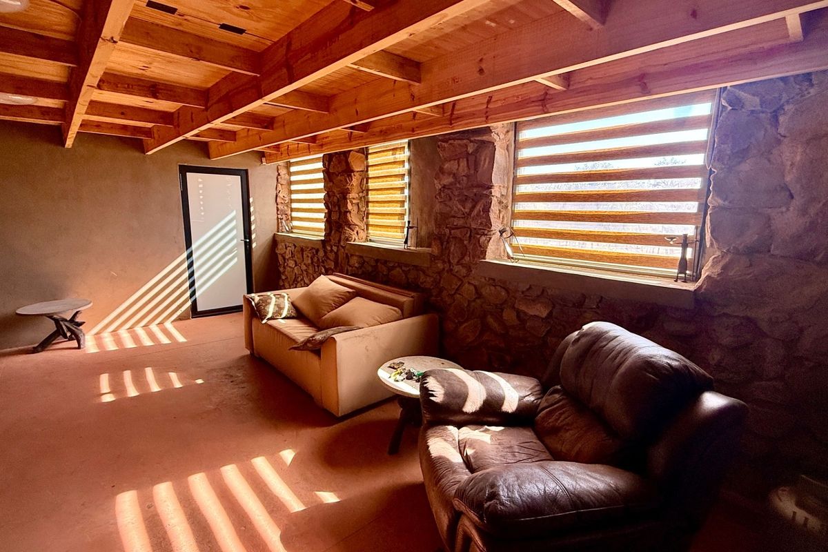 Rustic living area featuring exposed timber ceiling beams, natural stone wall construction, and modern roller blinds.