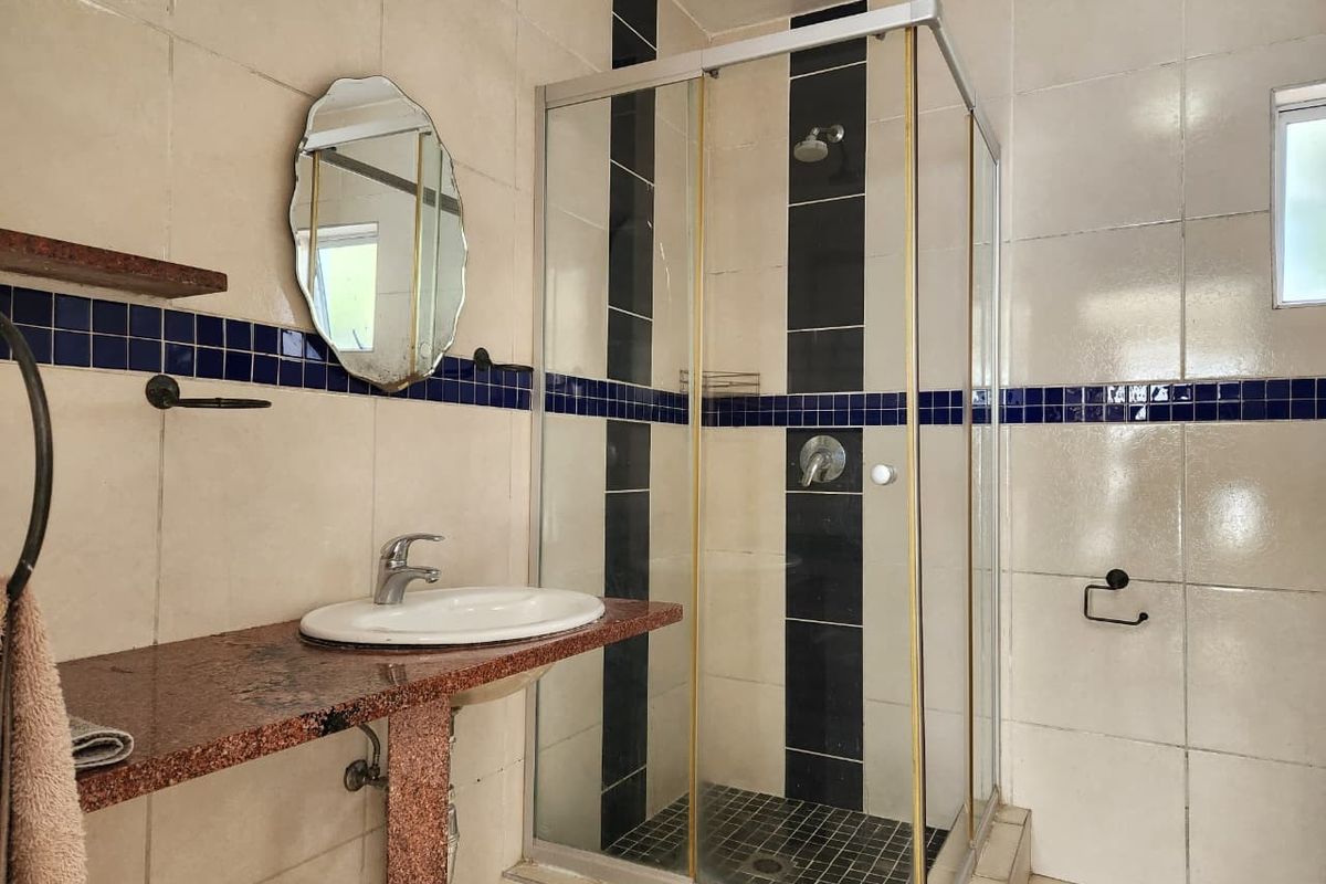 A functional bathroom featuring a corner shower enclosure, a granite-topped vanity with a basin, and decorative wall tiling.