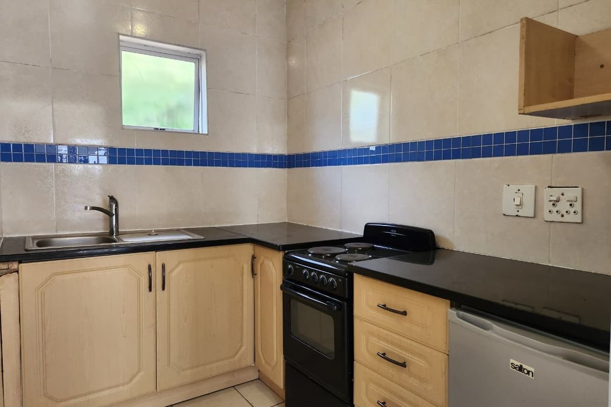 A functional kitchen featuring light wood cabinetry, black countertops, tiled walls with a decorative blue accent, and a built-in sink.