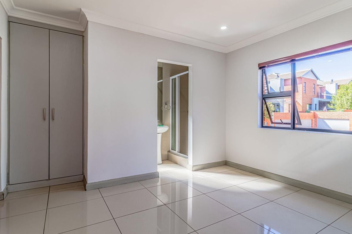 A bright, empty bedroom featuring tiled flooring, built-in cupboards, and an en-suite bathroom with a shower.