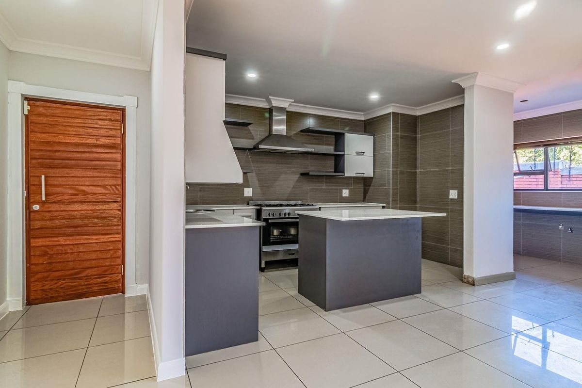 Modern kitchen featuring a central island, stainless steel gas stove with extractor fan, tiled backsplash, and sleek cabinetry, seamlessly integrated into an open-plan living space.