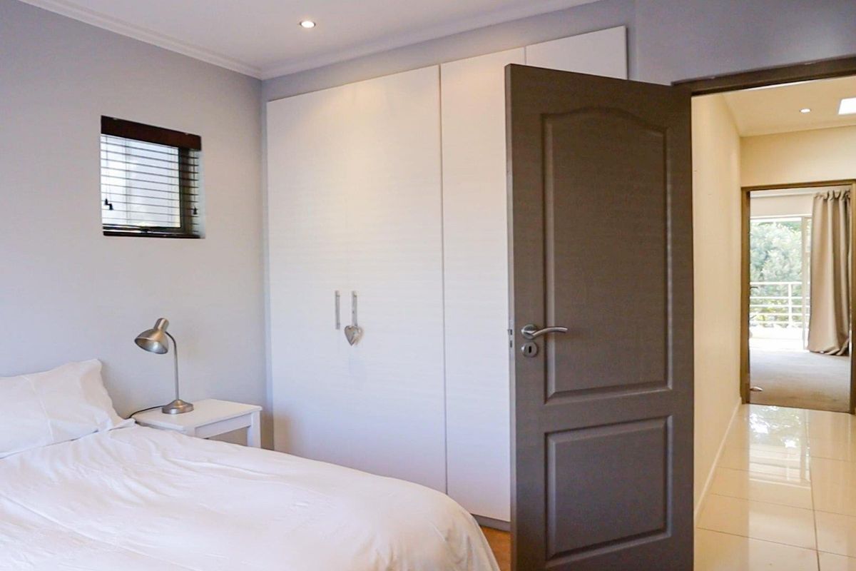 A well-maintained bedroom featuring built-in white cabinetry, recessed ceiling lighting, and a view through to the hallway and balcony.
