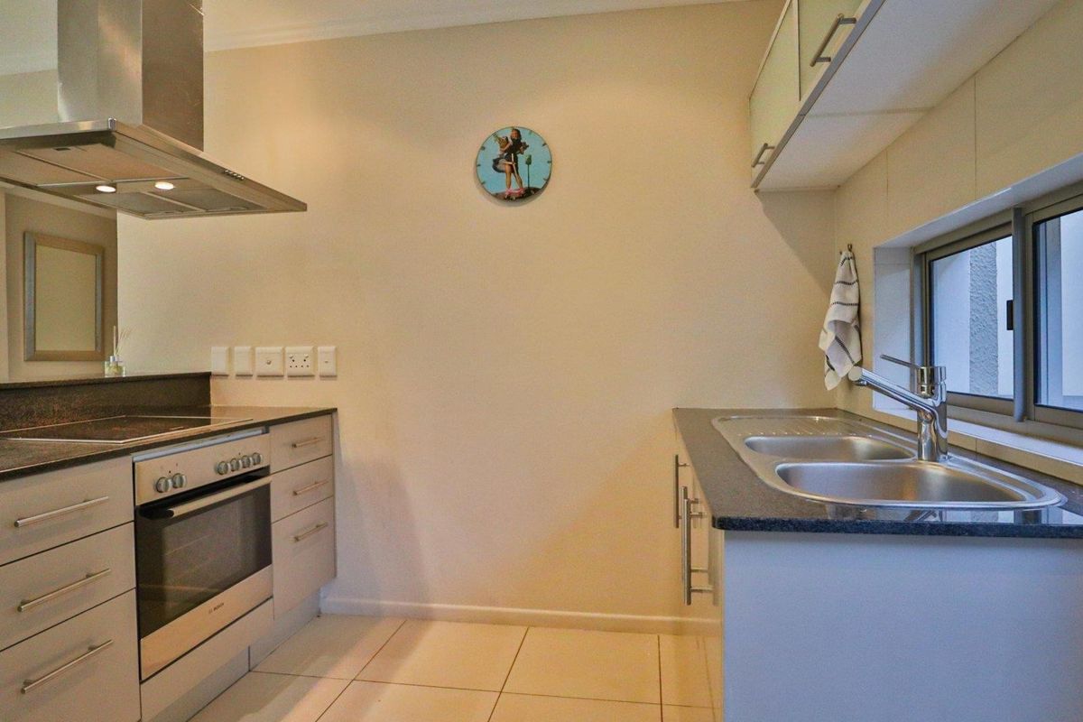 A functional kitchen featuring stone countertops, stainless steel double sink, built-in oven, electric hob, and stainless steel extractor fan.