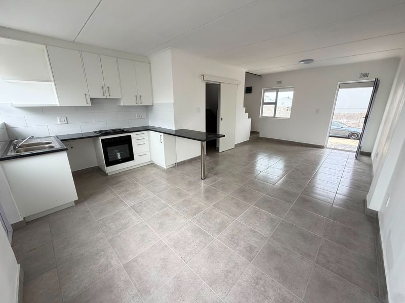 An open-plan kitchen and living area featuring modern white cabinetry, a built-in oven and hob, tiled flooring, and direct access to the exterior.