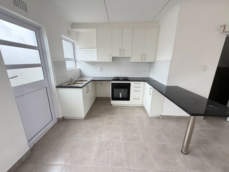 A clean, modern kitchen featuring white cabinetry, black granite countertops, a built-in oven and hob, and a convenient breakfast bar.