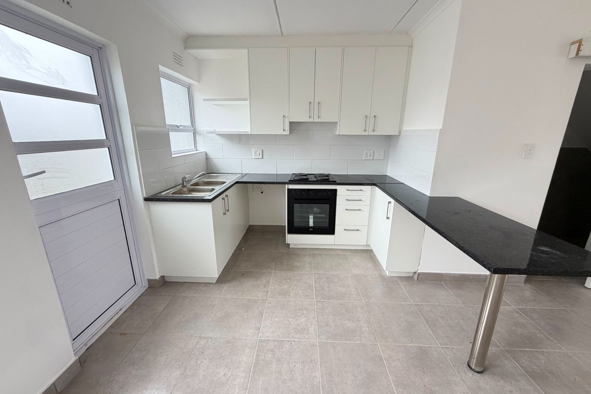 A clean, modern kitchen featuring white cabinetry, black granite countertops, a built-in oven and hob, and a convenient breakfast bar.